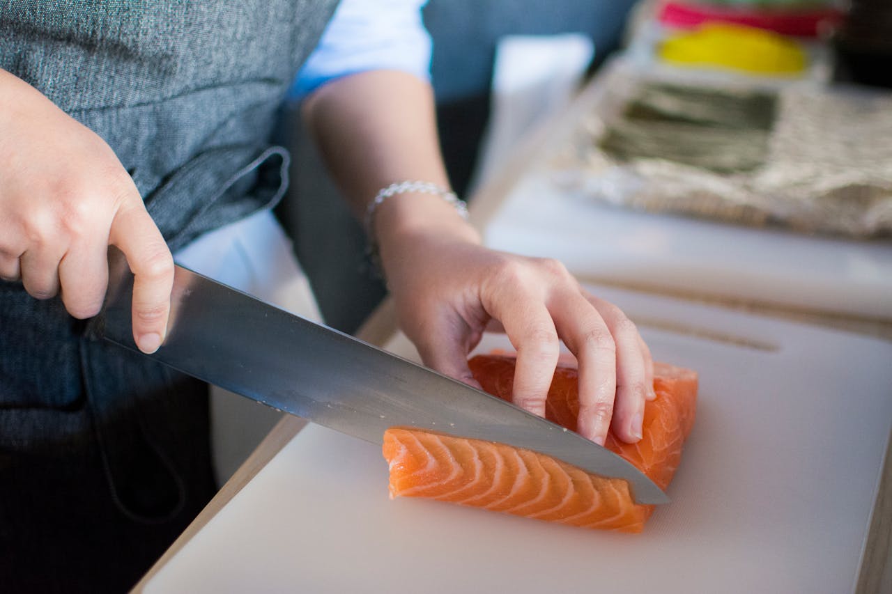 Close-up of a chefs hands slicing fresh salmon for sushi on a cutting board indoors.